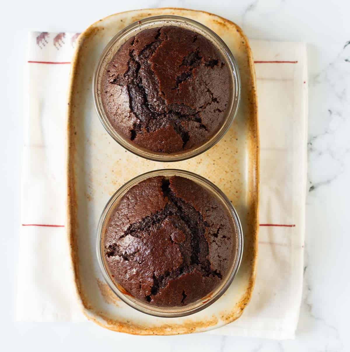baked chocolate cakes in 2 ramekins on a tray.