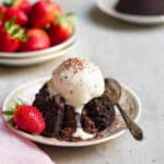 Chocolate lava cake with vanilla ice cream on top on a plate with a spoon.