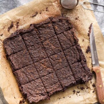 Miso brownies cut into 16 squares on parchment paper with a knife.