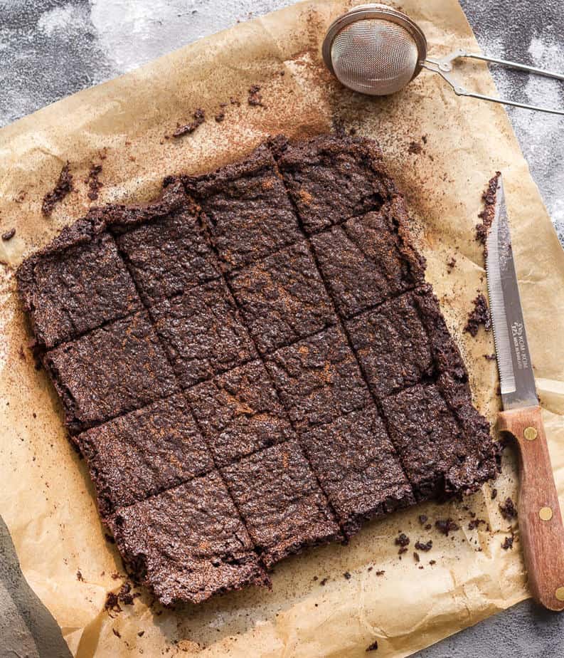 Miso brownies cut into 16 squares on parchment paper with a knife.