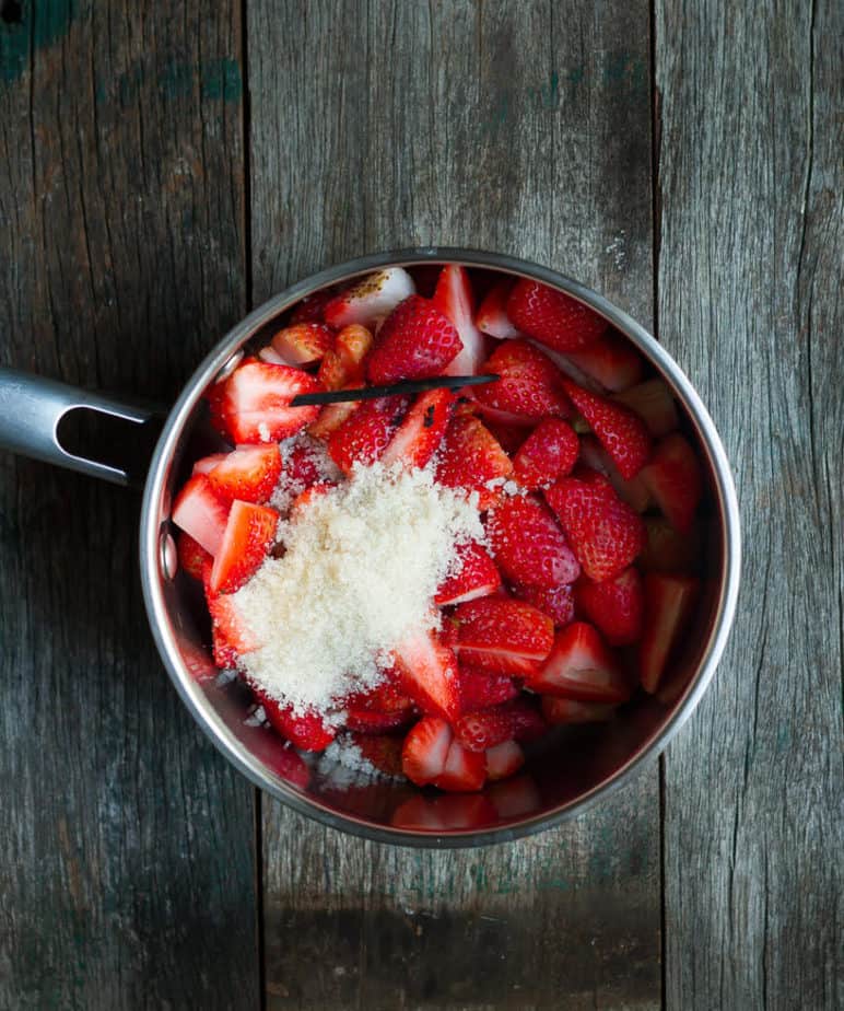 Chopped strawberries, raw sugar, and vanilla bean in a stainless steel saucepan.
