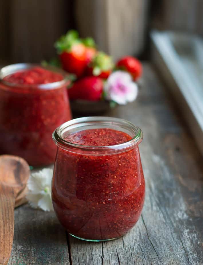 Strawberry chia seed jam in 2 glass jars with flowers in the background.