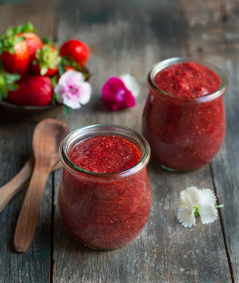 Strawberry chia jam in 2 glass jars with wooden spoons on the side.