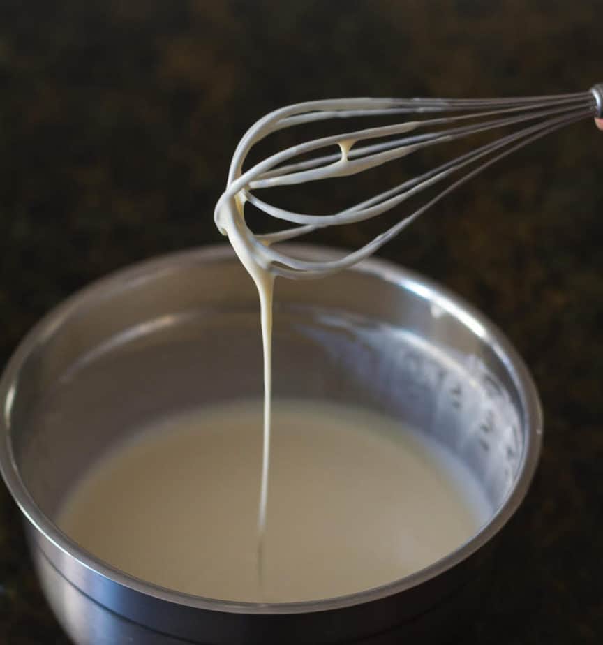 Batter for crepes dripping from a whisk into a bowl.