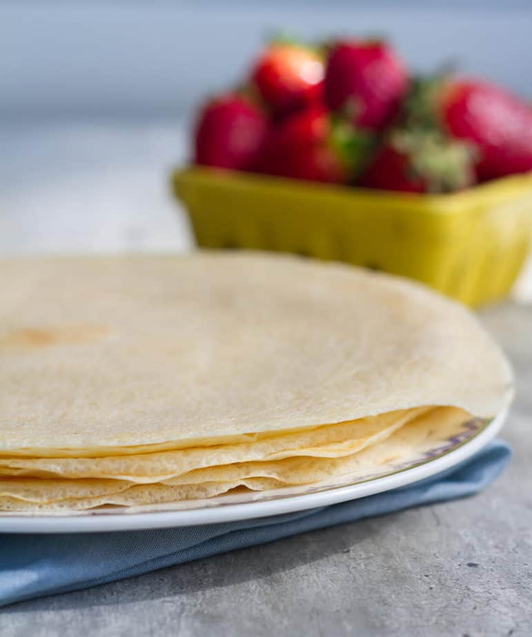 Crepes on a plate with strawberries sin the background.
