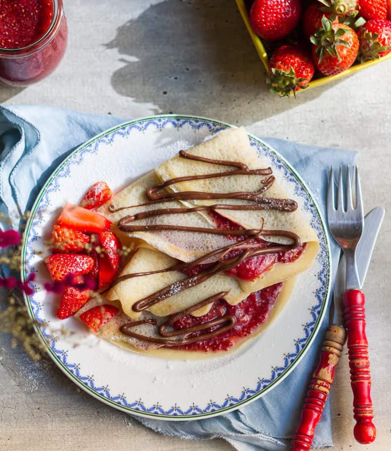 crepes filled with strawberry jam topped with chocolate sauce on a plate.