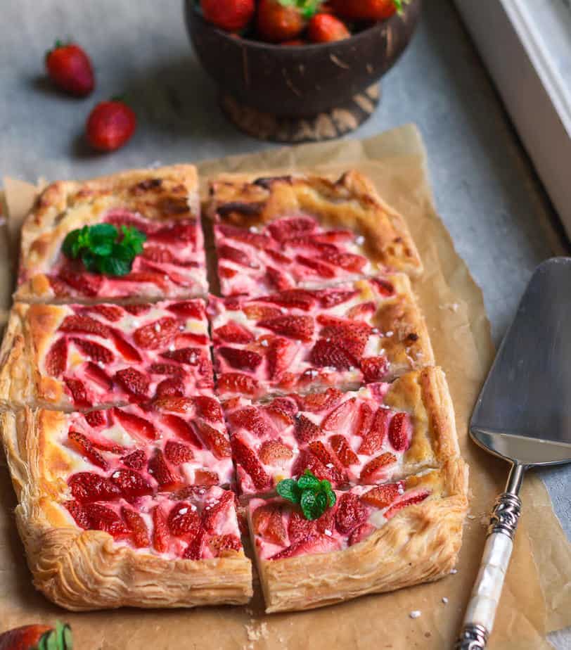 Strawberry tart cut into 8 pieces on parchment paper with a pie server on the side.