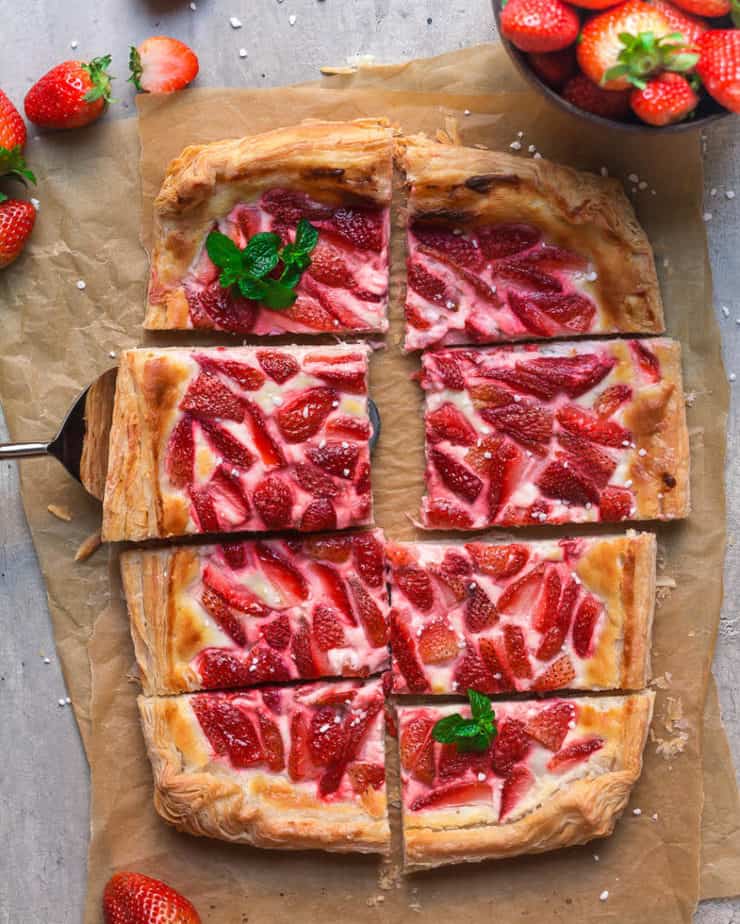 Strawberry tart cut into 8 pieces on parchment paper with a pie-server.
