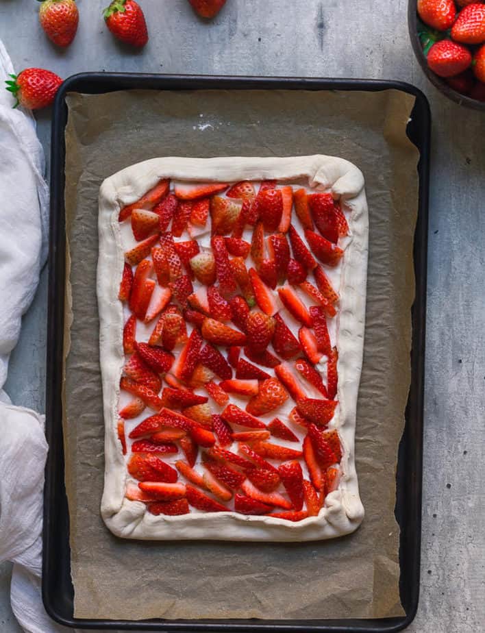Puff pastry with cream cheese and strawberries with edges crimped on a baking tray.