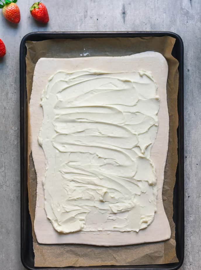 Rolle out puff pastry topped with cream cheese on a parchment-lined tray.