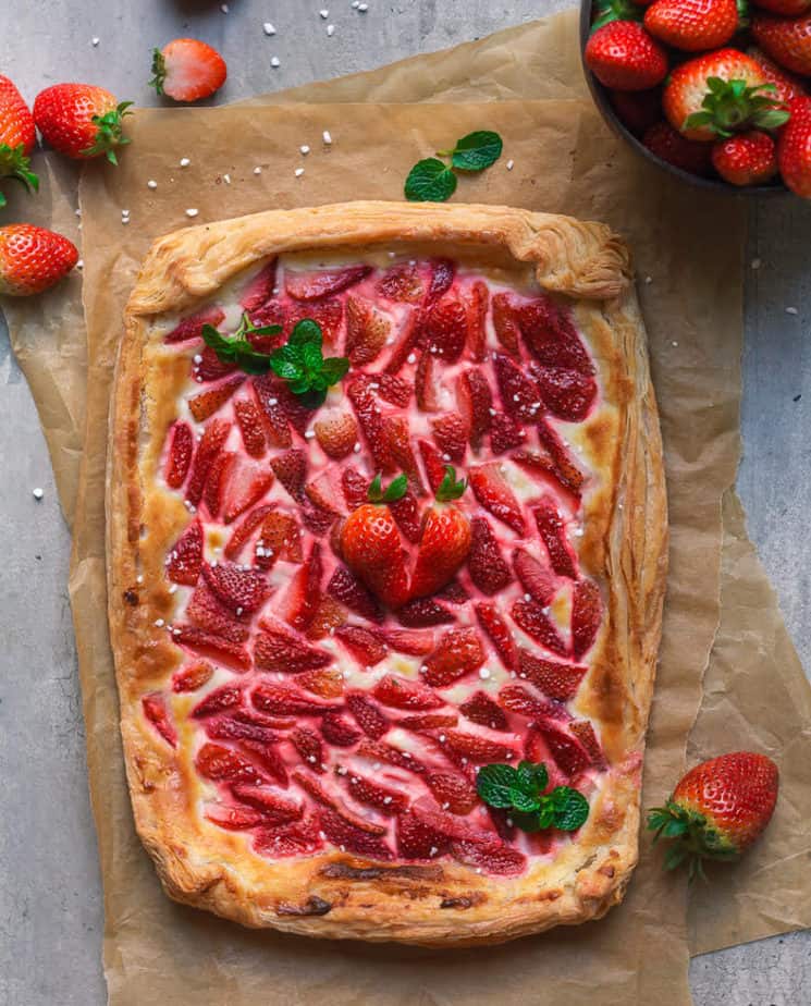 Baked strawberry puff pastry tart on parchment paper with fresh strawberries around.