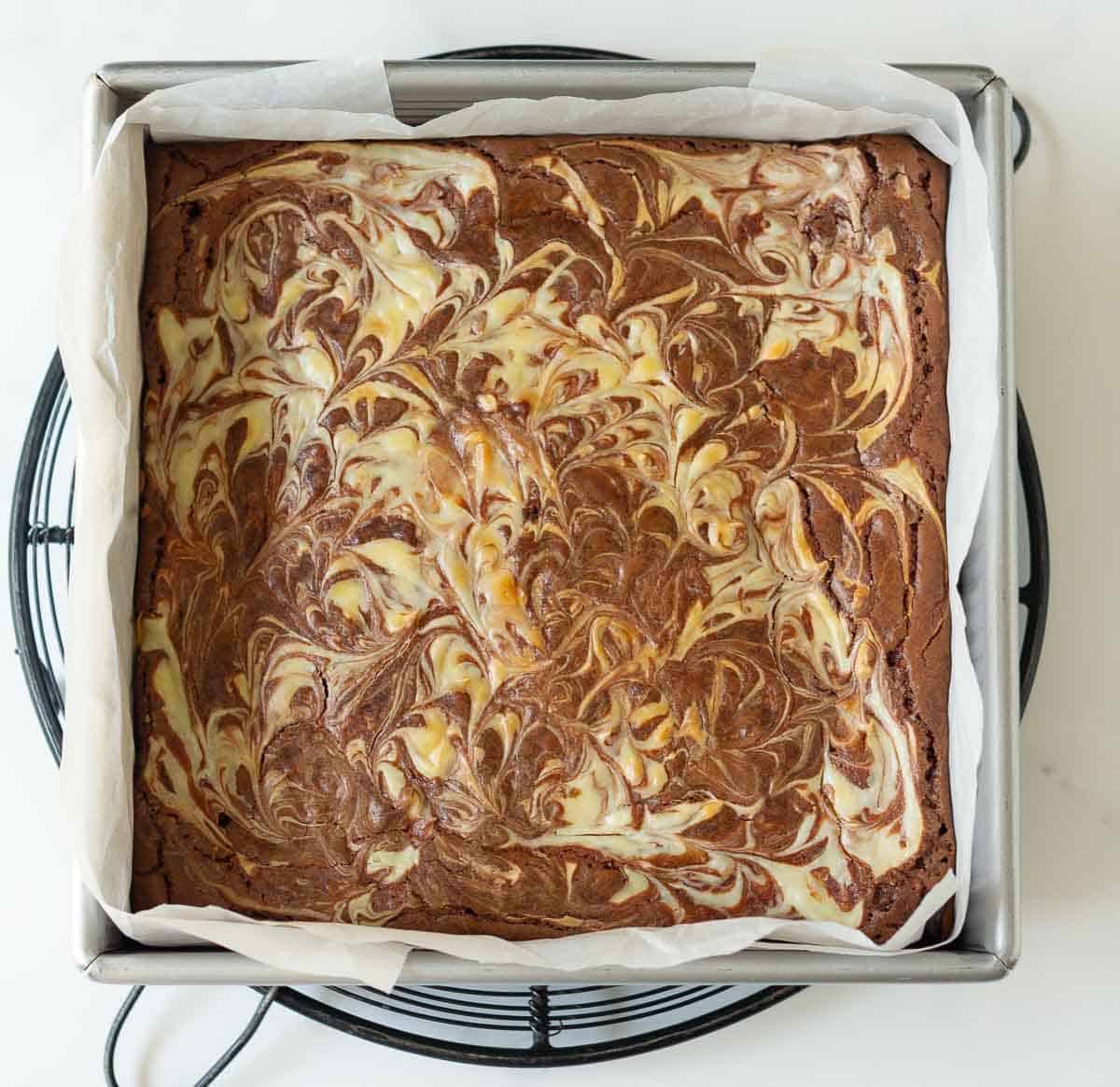 Baked cheesecake swirl brownies in a square pan lined with parchment paper.