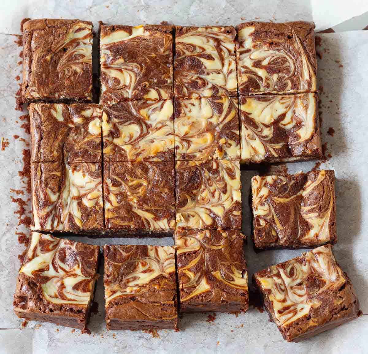 16 squares of cheesecake swirl brownies on parchment paper.