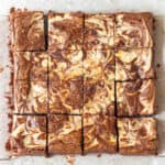 Cheesecake swirl brownies cut into 16 squares on parchment paper.