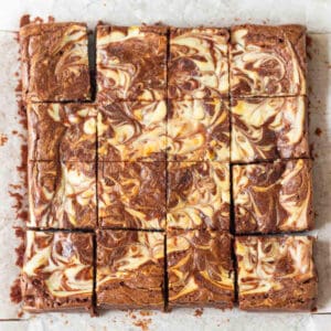 Cheesecake swirl brownies cut into 16 squares on parchment paper.