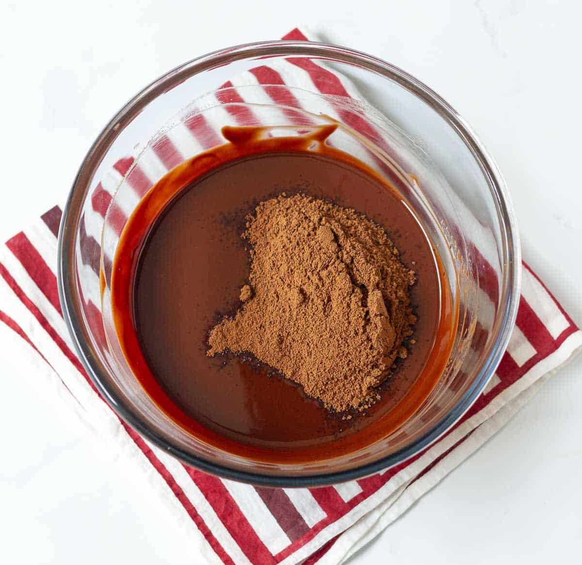 Cocoa powder on top of melted chocolate in a mixing bowl.