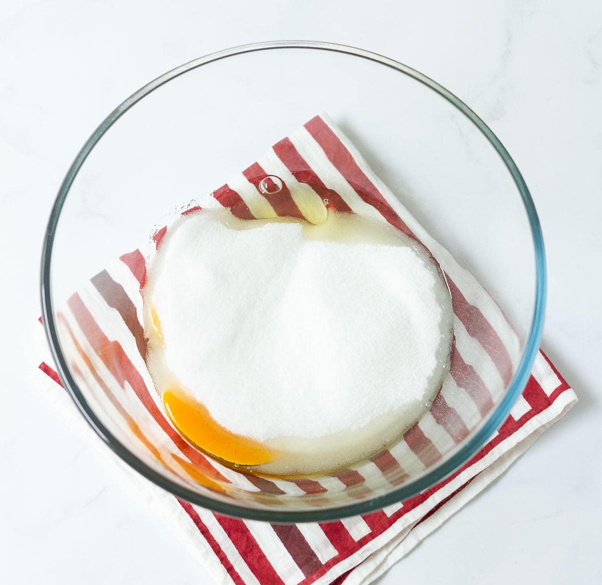 Eggs and sugar in a mixing bowl on a red and white stripe napkin.