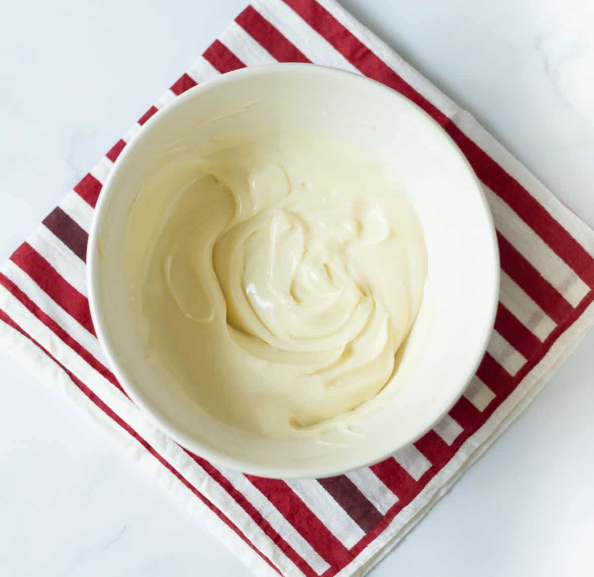 Cheesecake batter in a bowl on top of red and white striped napkin.