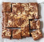 16 squares of cheesecake swirl brownies on parchment paper.