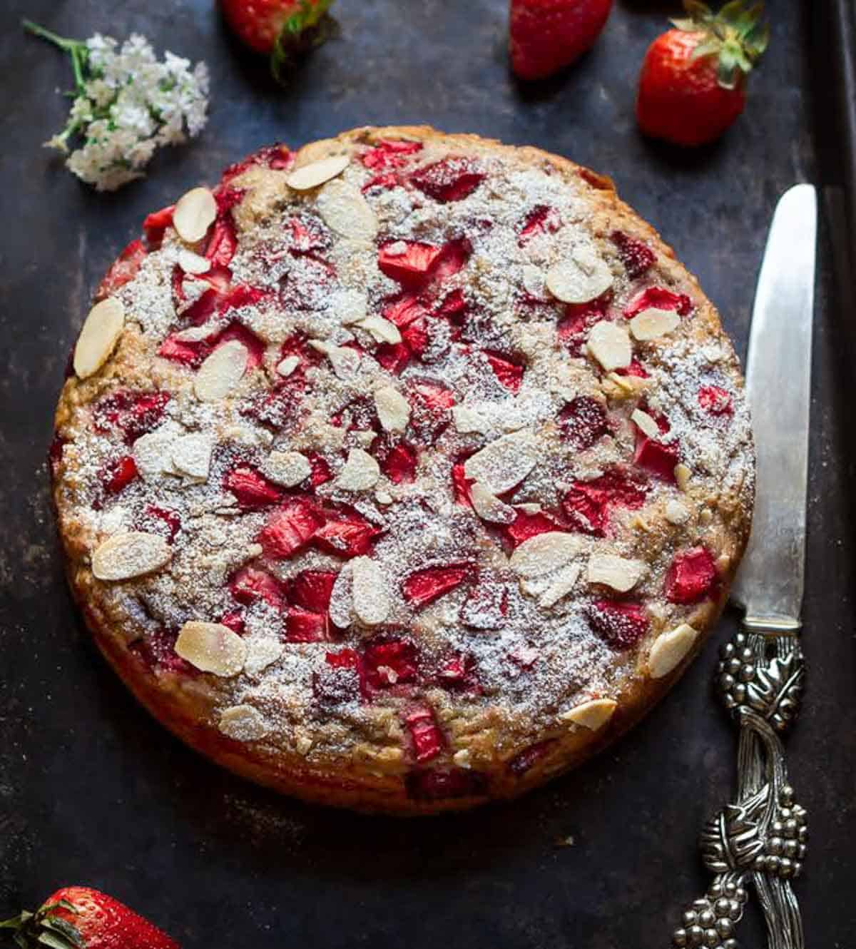 Strawberry jam cake on a black tray with a cake knife on the side.