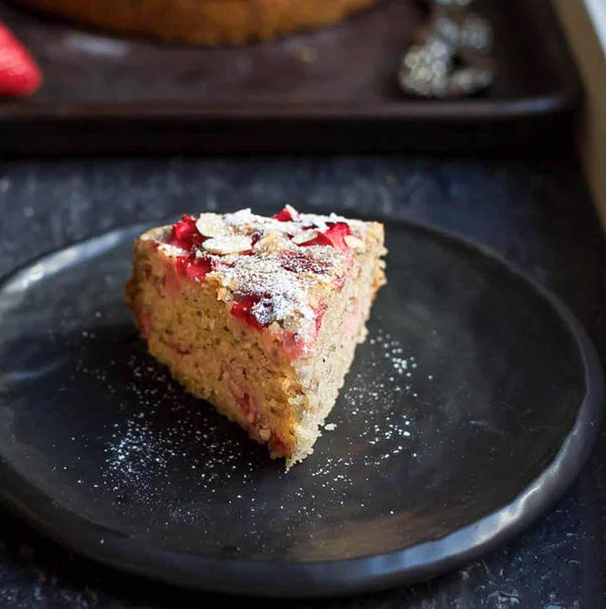 A slice of strawberry cake on a small black plate.