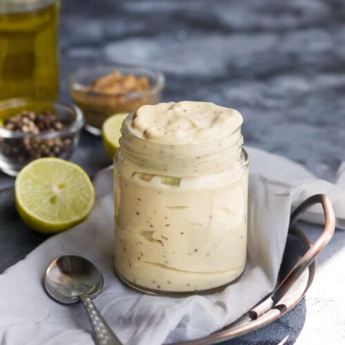 vegan mayonnaise in a glass jar with a spoon and ingredients in the background.