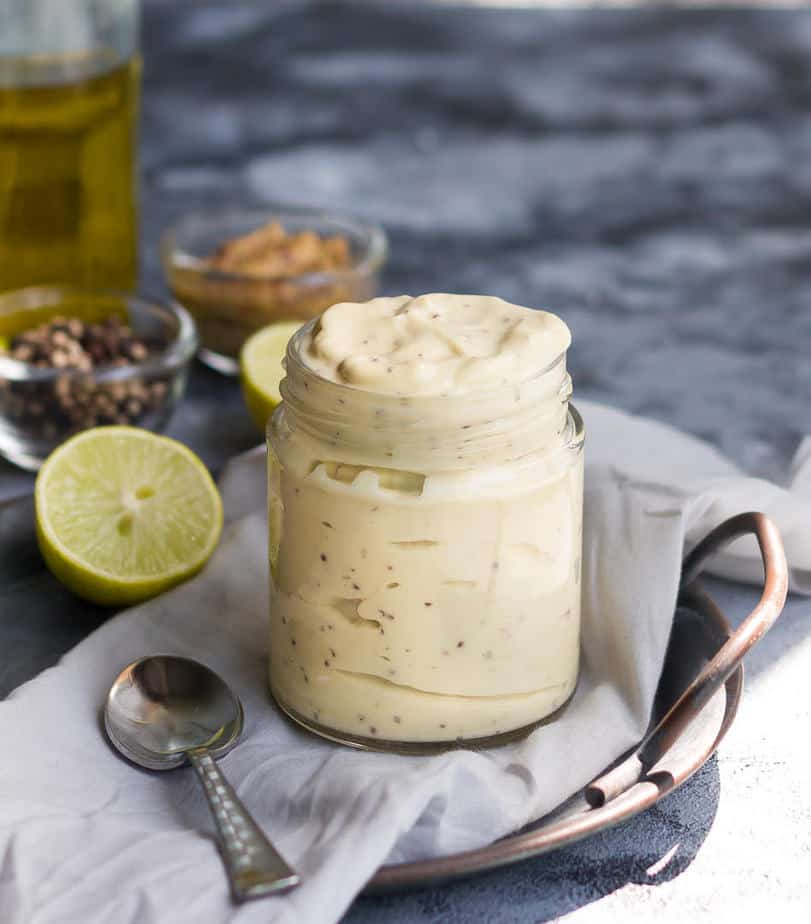 vegan mayonnaise in a glass jar with a spoon and ingredients in the background.
