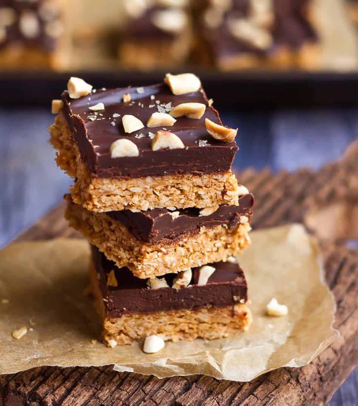 3 peanut butter chocolate bars stacked on parchment paper on a wooden surface.
