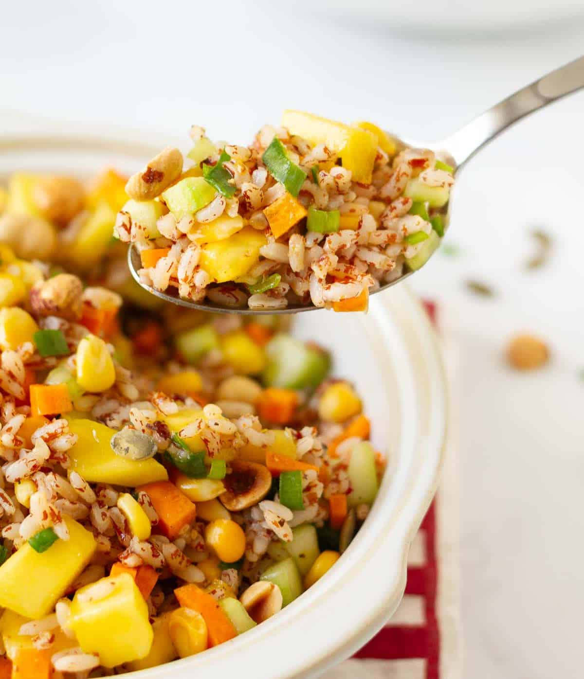 A spoon of rice and mango salad on top of a bowl of salad.