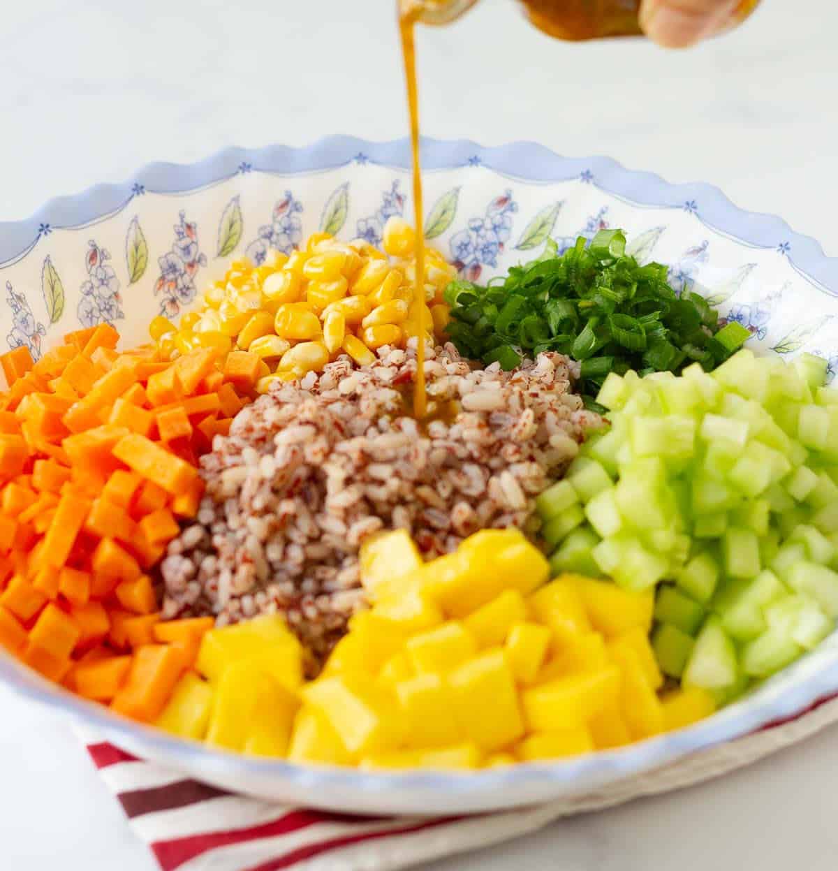 Salad dressing being poured into a bowl of vegetables and rice.