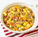 A bowl of rice and mango salad on a red and white napkin.
