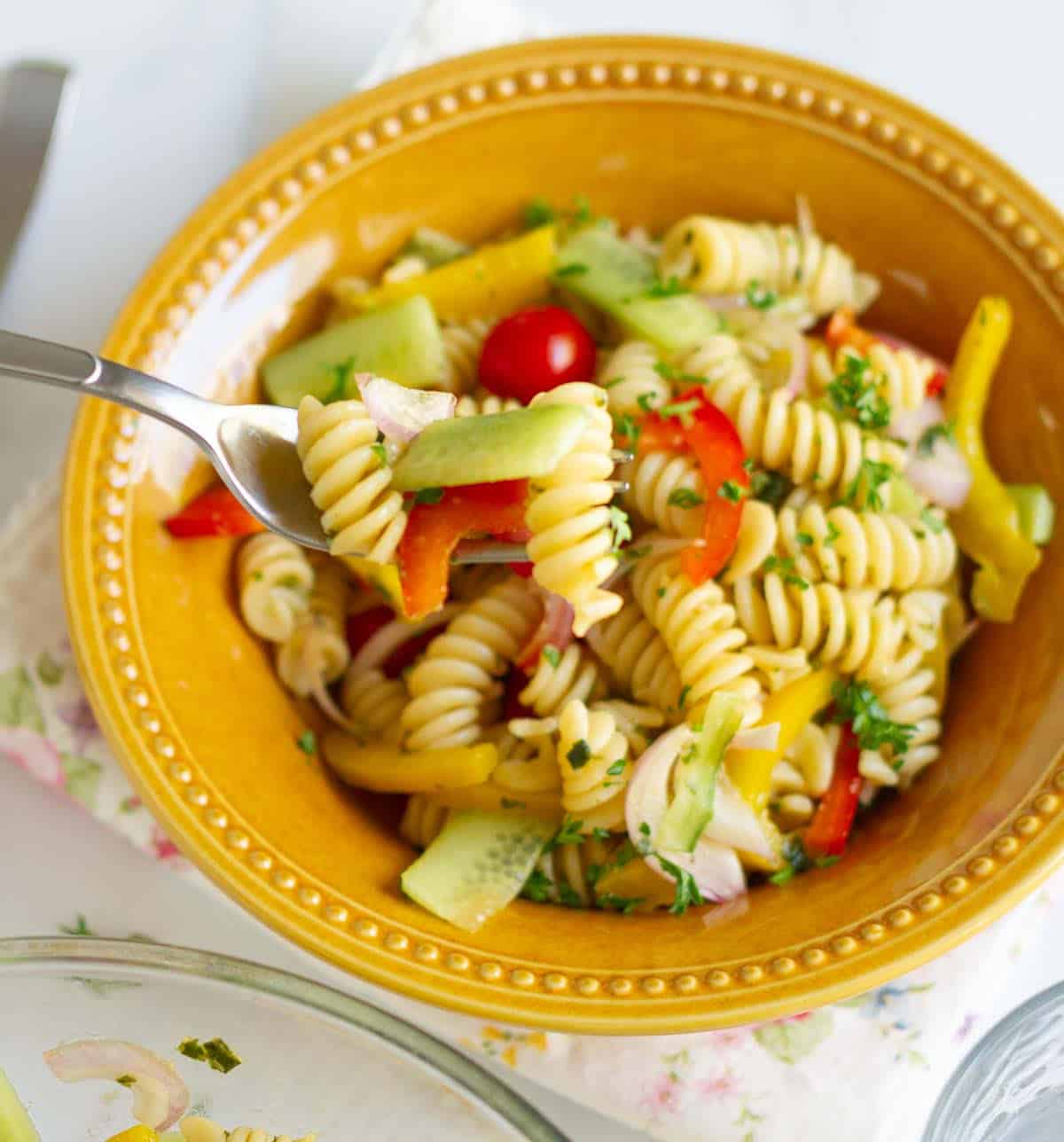 A fork full of pasta salad on top of bowl of salad.