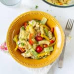 Pasta salad with veggies in a yellow bowl, with a fork on the side.