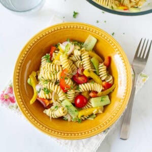 Pasta salad with veggies in a yellow bowl, with a fork on the side.
