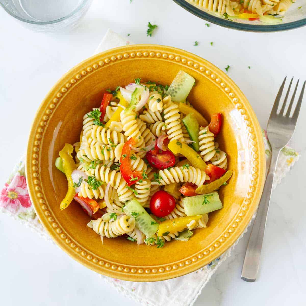 Pasta salad with veggies in a yellow bowl, with a fork on the side.