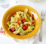 Pasta salad with veggies in a yellow bowl with a fork on the side.