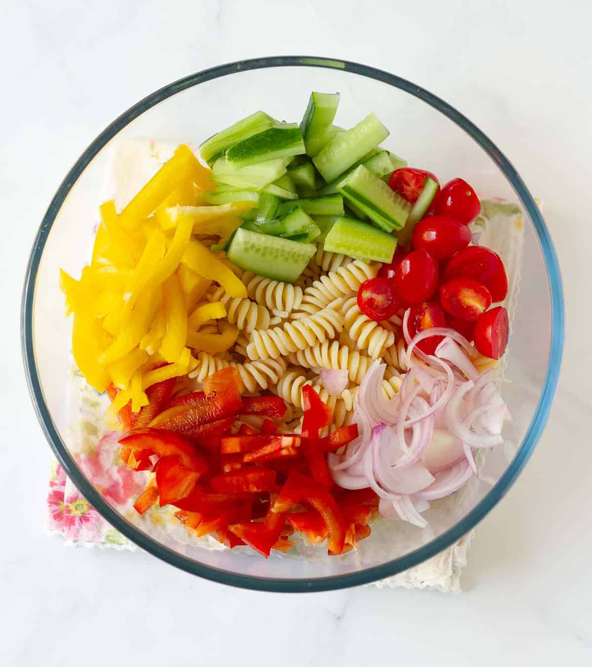 A bowl with pasta, cucumbers, onions, cherry tomatoes, red and yellow peppers.