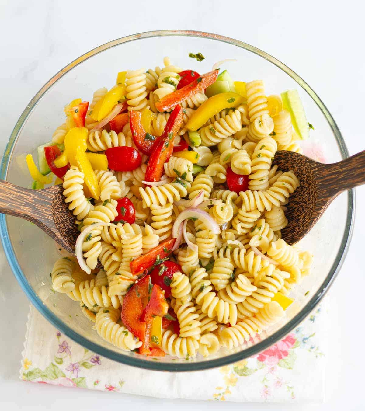 Pasta salad getting tossed with dressing using 2 wooden spoons.