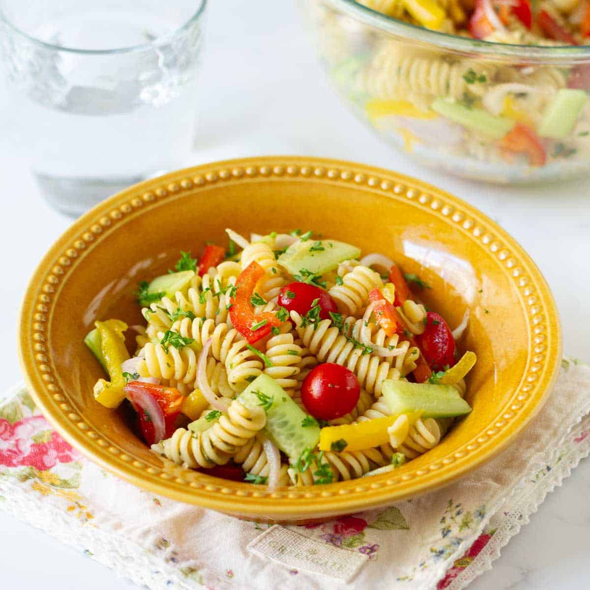 A bowl of pasta and veggie salad with a fork & a glass of water on the side.