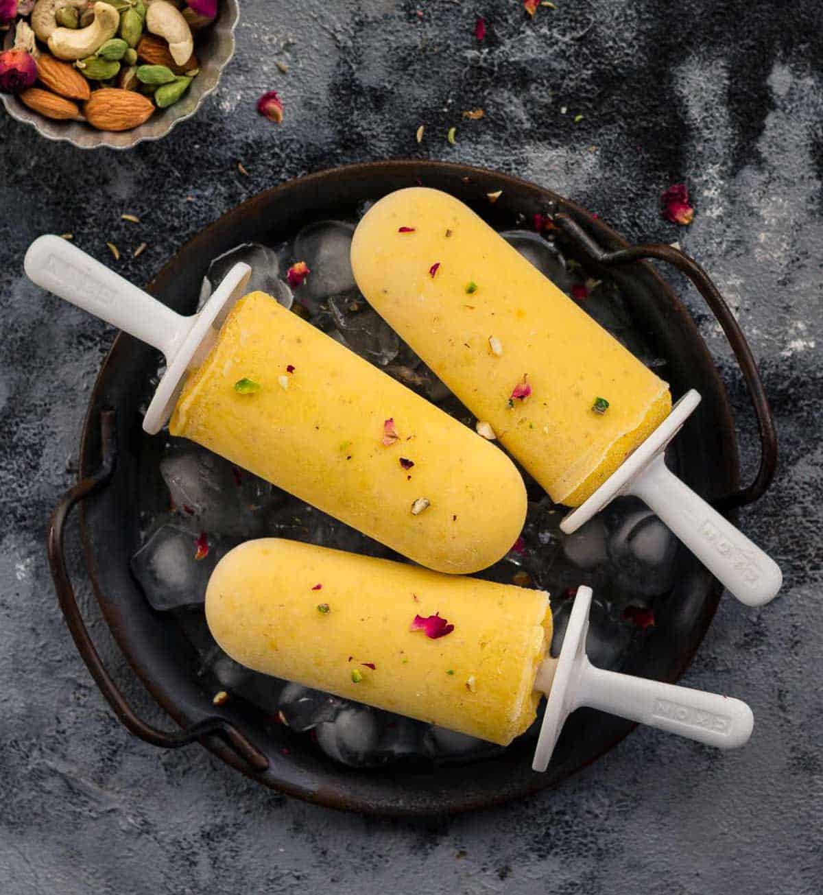 3 mango popsicles on an ice-filled tray.