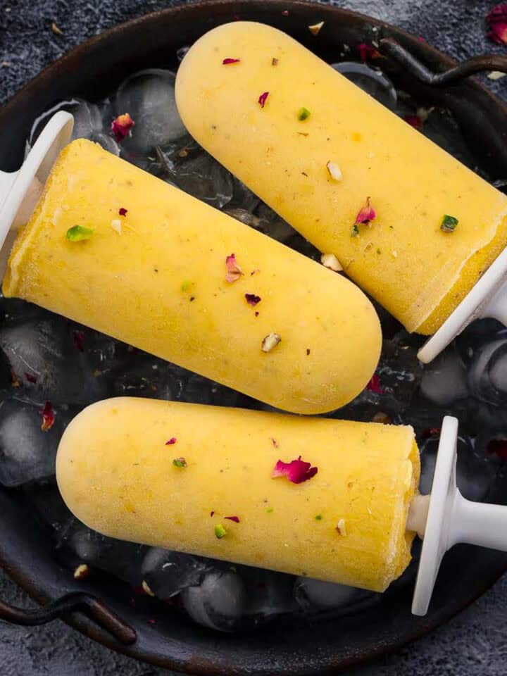 3 mango popsicles on a iced filled tray.