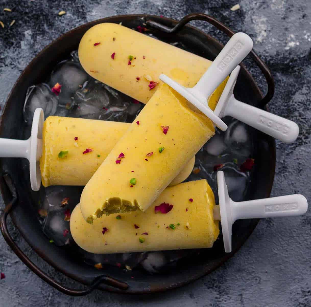 3 mango popsicles on a tray and 1 popsicle with bite taken placed on top.
