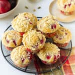 Plum muffins with streusel stacked on a round wire rack.