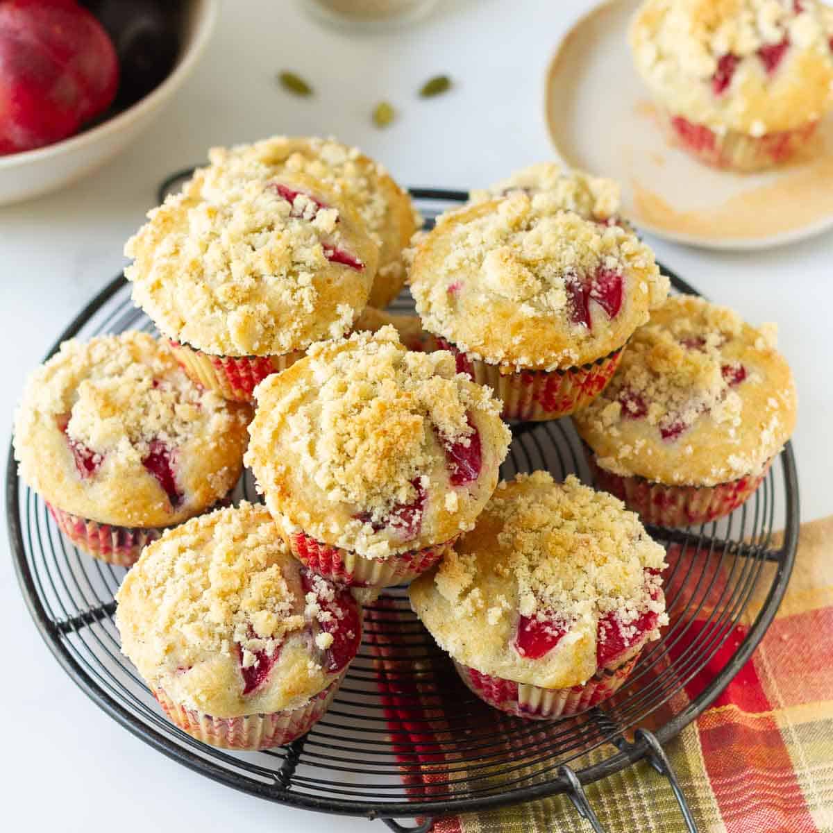 Plum muffins with streusel stacked on a round wire rack.