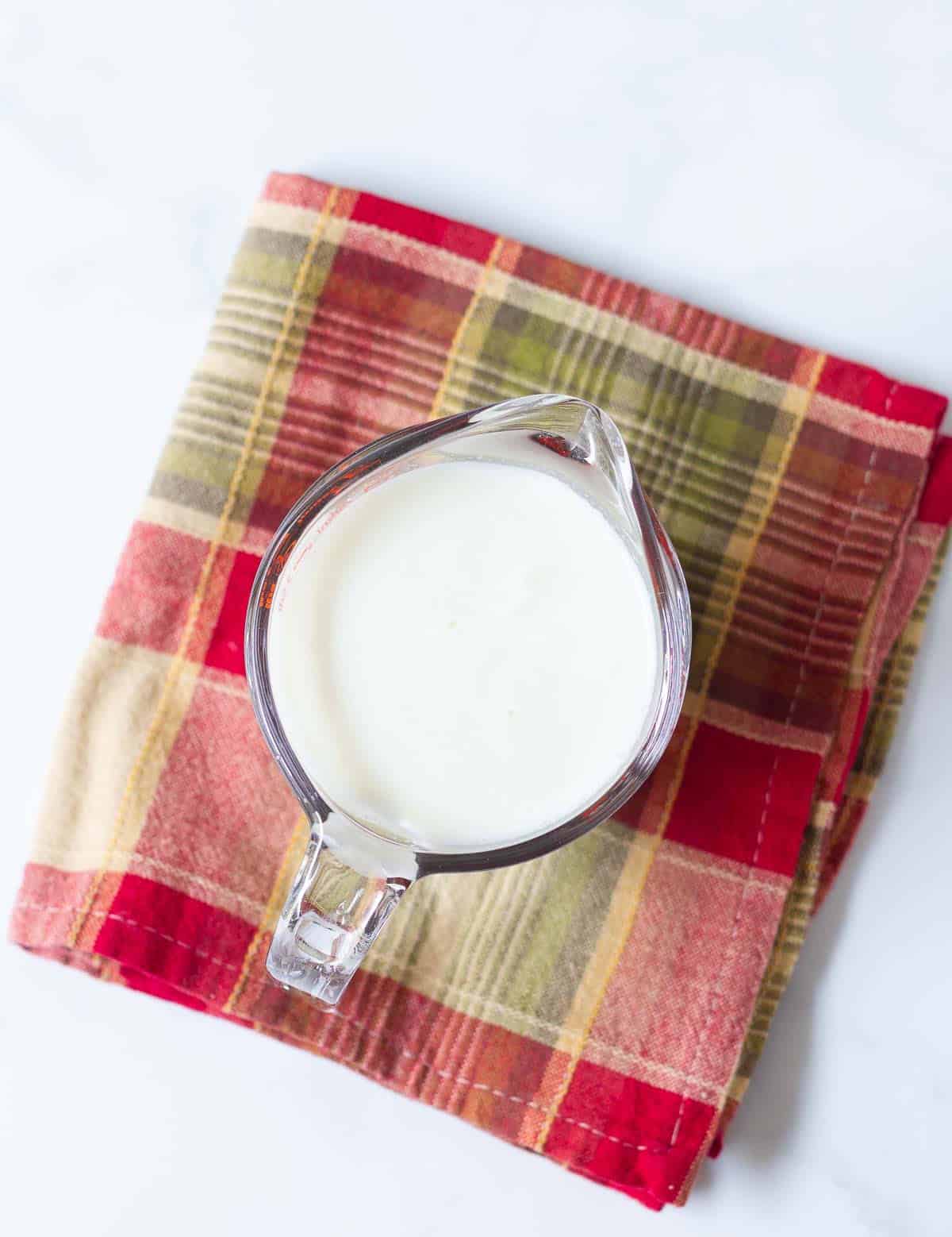 Milk in a measuring cup on a chequered napkin.
