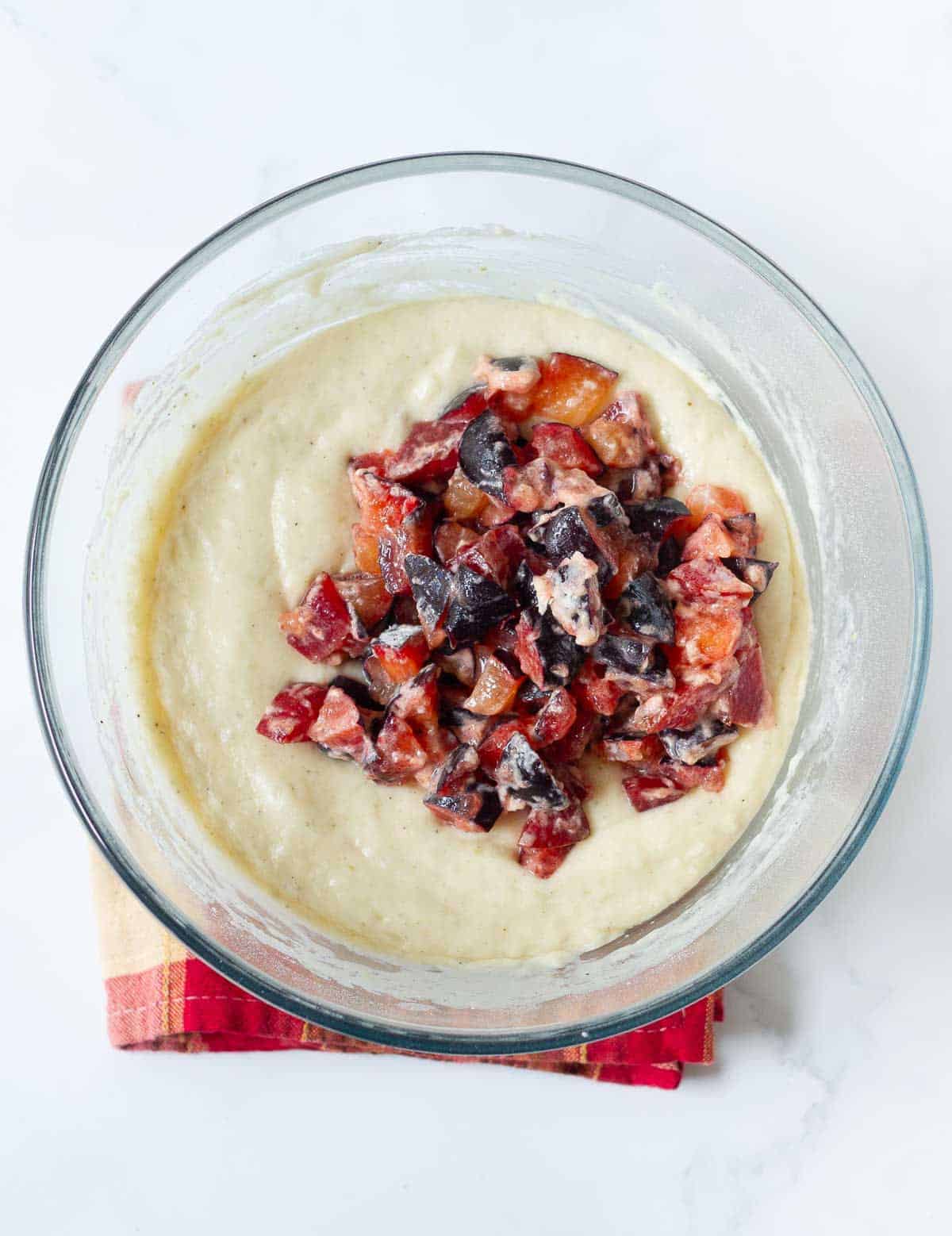 Diced plums coated in flour on top of batter in a bowl.