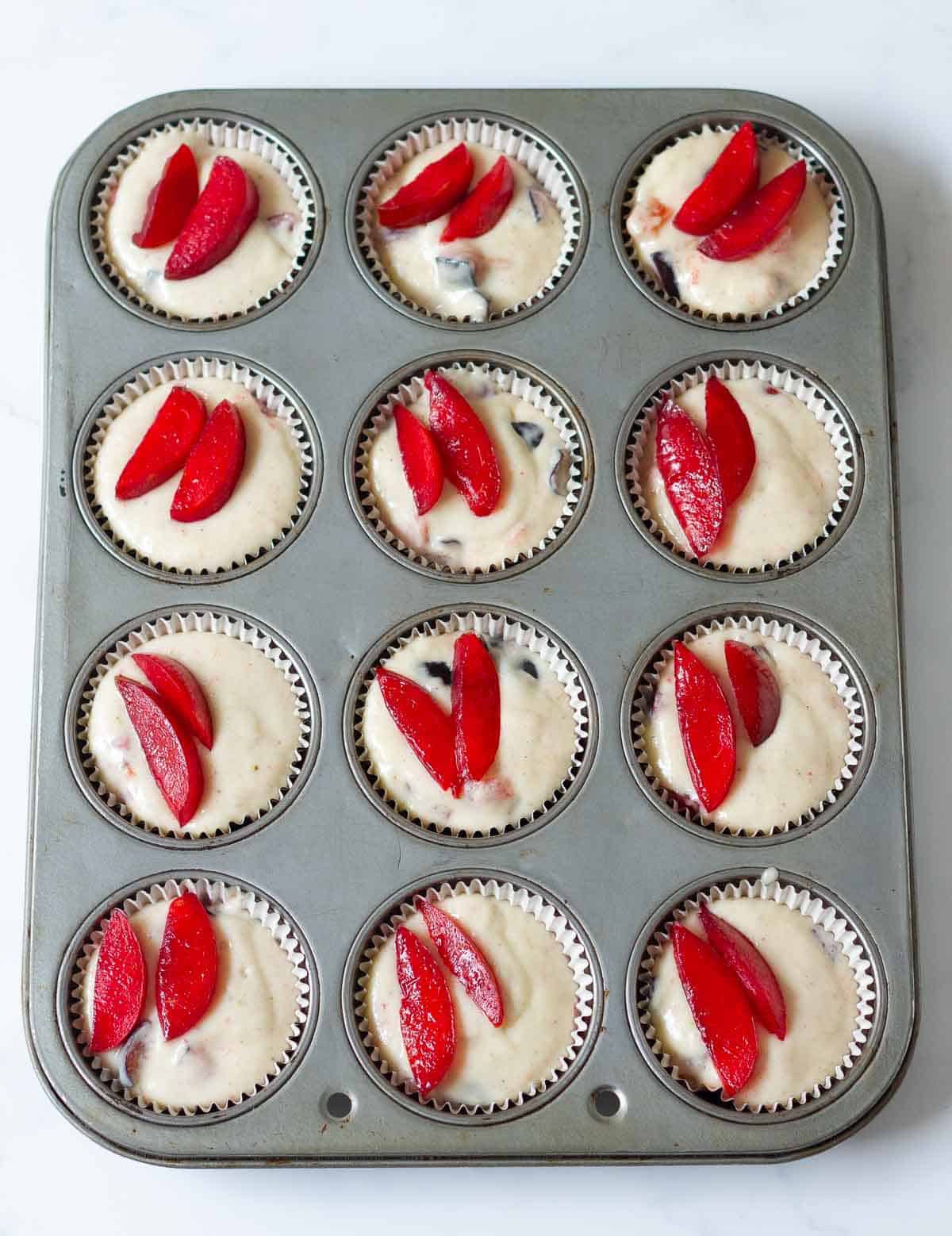 Muffin tray filled with batter that is topped with plum slices.