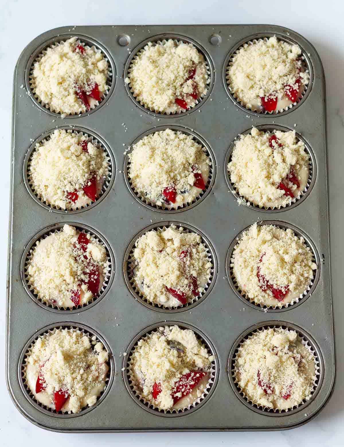 Muffin batter topped with streusel in a muffin tray.