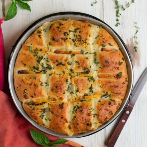 Cheesy Garlic Bread in a round cake pan with a knife on the side.