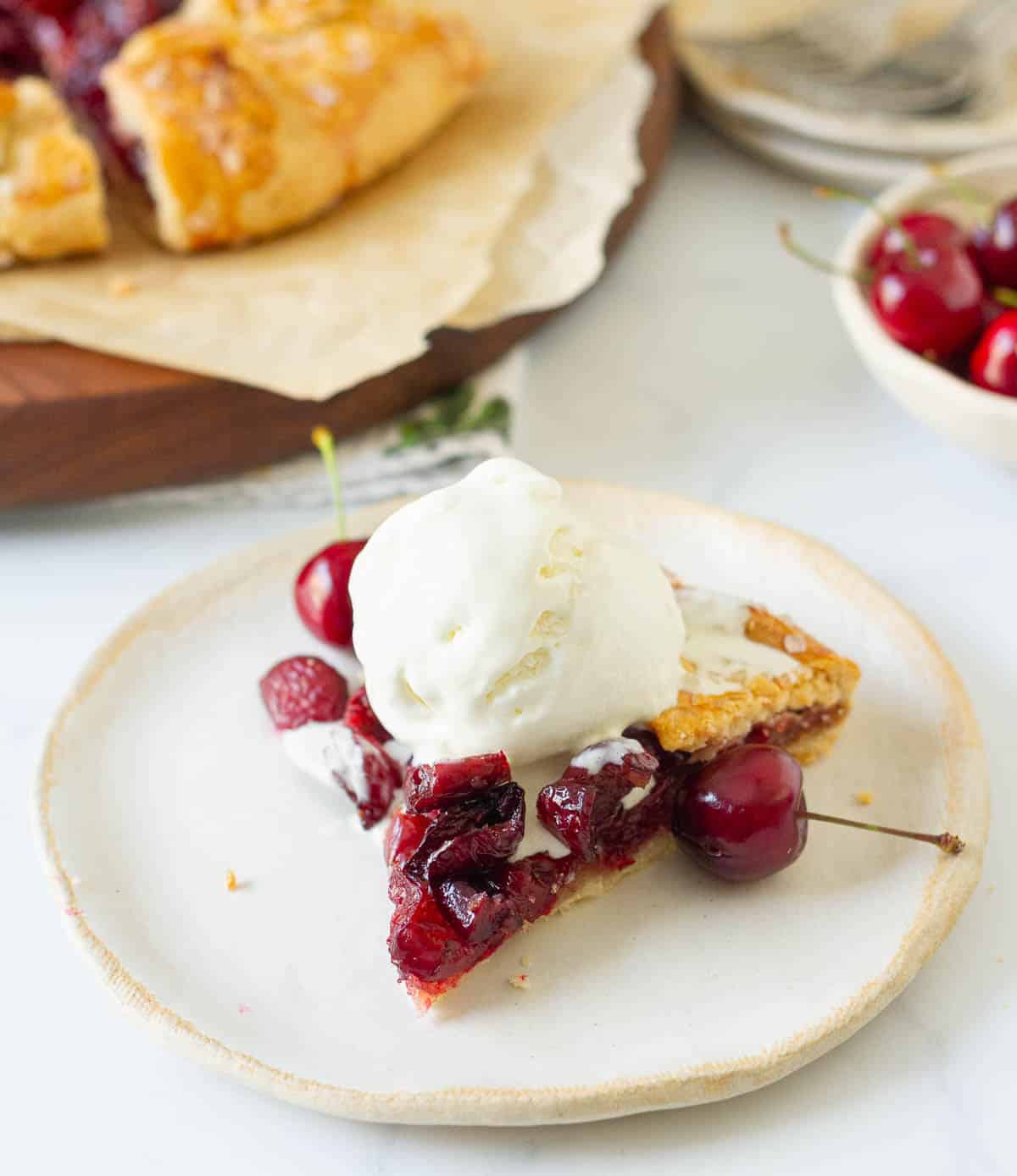 A slice of cherry galette with a scoop of vanilla ice cream on a plate.